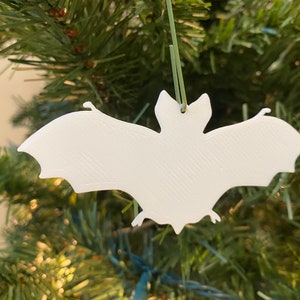 Può includere: Addobbo natalizio bianco a forma di pipistrello appeso a un albero di Natale artificiale verde.