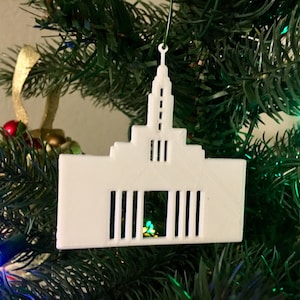 May include: White 3D printed Christmas ornament shaped like a church building. The ornament has a spire and windows.