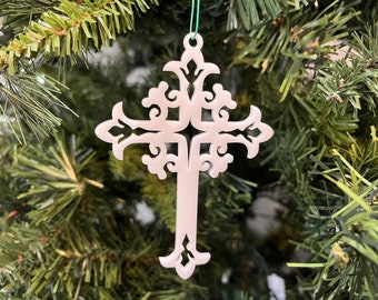 Könnte beinhalten: Ein weißer, verzierter Weihnachtsbaumschmuck in Form eines Kreuzes mit einem filigranen, komplizierten Design. Der Schmuck hängt an einer grünen Schnur an einem Weihnachtsbaum.