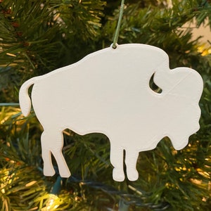 May include: White ceramic ornament shaped like a buffalo, hanging on a green Christmas tree.