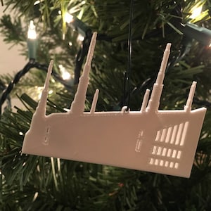 May include: White 3D printed Christmas bauble shaped like a building with multiple towers. The bauble is hanging from a Christmas tree.