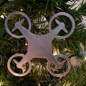 May include: A silver-colored drone ornament for a Christmas tree. The ornament is shaped like a drone with four propellers.