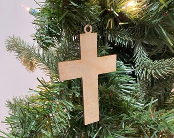 Könnte beinhalten: Ein hölzerner Kreuz-Anhänger in natürlicher Holzfarbe, der an einem grünen Weihnachtsbaum hängt.