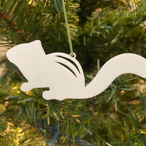 May include: White, cutout, chipmunk Christmas ornament hanging on a green artificial Christmas tree.
