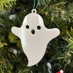 May include: White ghost-shaped Christmas bauble with a simple face, hanging on a green artificial Christmas tree.