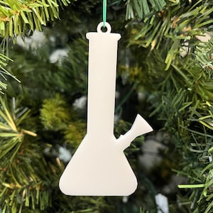 Op de afbeelding: Witte kerstversiering van keramiek in de vorm van een bong. De versiering hangt aan een groen touwtje aan een kerstboom.
