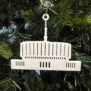 Può includere: Addobbo in legno bianco, tagliato al laser, a forma di edificio con una cupola in cima. L'addobbo è appeso a un albero di Natale.