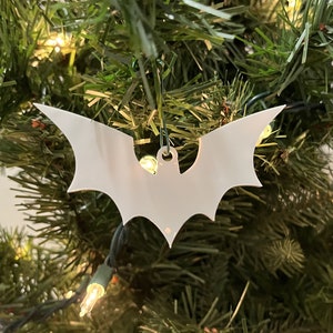 Può includere: Ciondolo a forma di pipistrello in carta bianca appeso a un albero di Natale artificiale verde con luci bianche.
