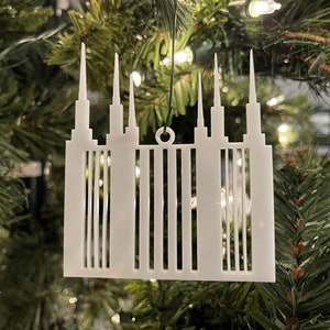 Może przedstawiać: Biała, wycinana laserowo ozdoba w kształcie świątyni z wieloma wieżami. Ozdoba wisi na choince.