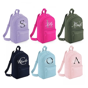 May include: Six personalised backpacks in different colours, each with a name embroidered on the front. The backpacks are purple, pink, green, blue, light blue, and navy blue.