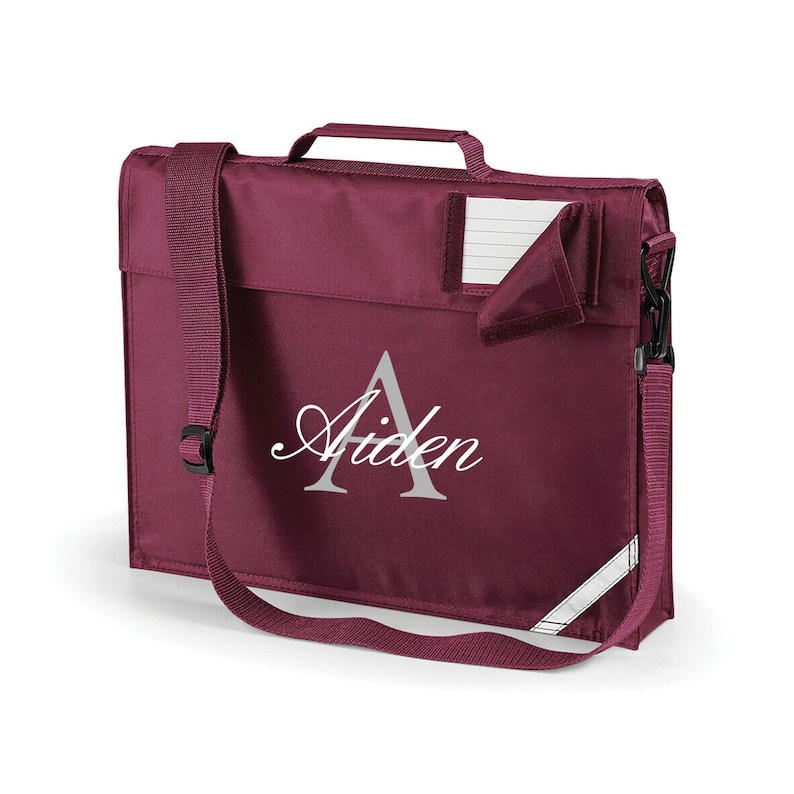 Pu&ograve; includere: Zaino scolastico color borgogna con una tracolla regolabile e una piccola tasca sul davanti. Lo zaino &egrave; personalizzato con la lettera "A" e il nome "Aiden" in un font argentato.
