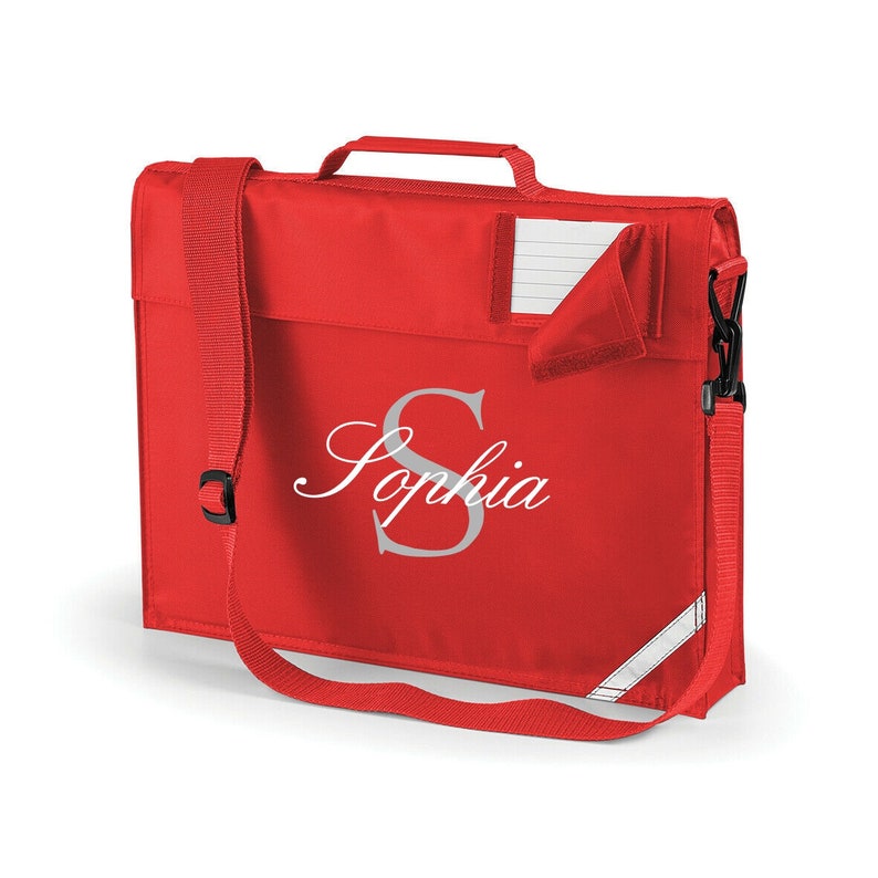 Pu&ograve; includere: Zaino rosso con una tracolla bianca e un nome bianco "Sophia" con un'iniziale "S" grigia. Lo zaino ha una piccola tasca sul davanti.