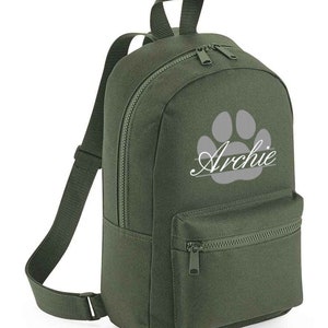 May include: A green canvas backpack with a grey paw print and the name "Archie" in white lettering. The backpack has a zipped front pocket.