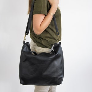 May include: A black leather hobo bag with a soft, slouchy silhouette and a wide shoulder strap. The bag features antique brass-toned metal hardware, including swivel clips that attach the strap to the sides of the bag.