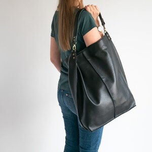 K&ouml;nnte beinhalten: Eine gro&szlig;e schwarze Ledertasche mit einem langen Trageriemen. Die Tasche hat eine strukturierte Form und ist aus strukturiertem Leder gefertigt.