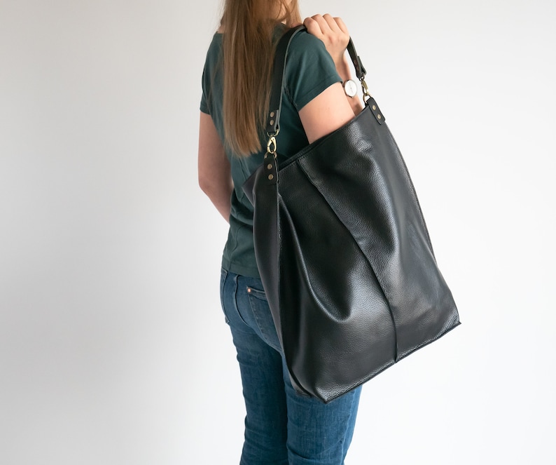 K&ouml;nnte beinhalten: Eine gro&szlig;e schwarze Ledertasche mit einem langen Trageriemen. Die Tasche hat eine strukturierte Form und ist aus strukturiertem Leder gefertigt.
