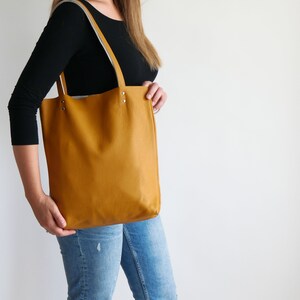May include: A mustard yellow leather tote bag with a white leather trim and silver hardware. The bag has a spacious interior and is perfect for everyday use.