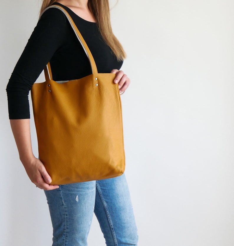 May include: A mustard yellow leather tote bag with a white leather trim and silver hardware. The bag has a spacious interior and is perfect for everyday use.