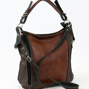 Pode incluir: Uma bolsa de m&atilde;o de couro marrom e preto com uma al&ccedil;a longa para o ombro. A bolsa tem um bolso com z&iacute;per na frente e um fecho de aba.