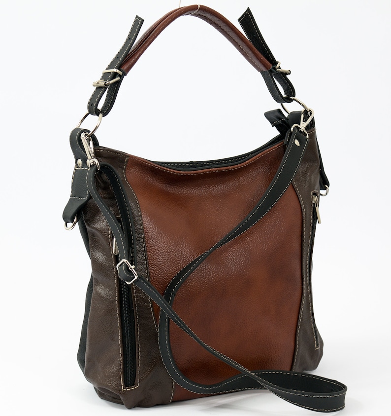 Pode incluir: Uma bolsa de m&atilde;o de couro marrom e preto com uma al&ccedil;a longa para o ombro. A bolsa tem um bolso com z&iacute;per na frente e um fecho de aba.