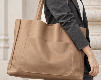 Könnte beinhalten: Eine große, hellbraune Tragetasche mit glatter, matter Oberfläche und einer auffälligen rechteckigen Vordertasche. Die Tasche verfügt über zwei lange Schulterriemen und sichtbare Nähte an den Kanten der Tasche.