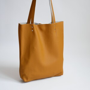 May include: A mustard yellow leather tote bag with two straps and silver rivets.