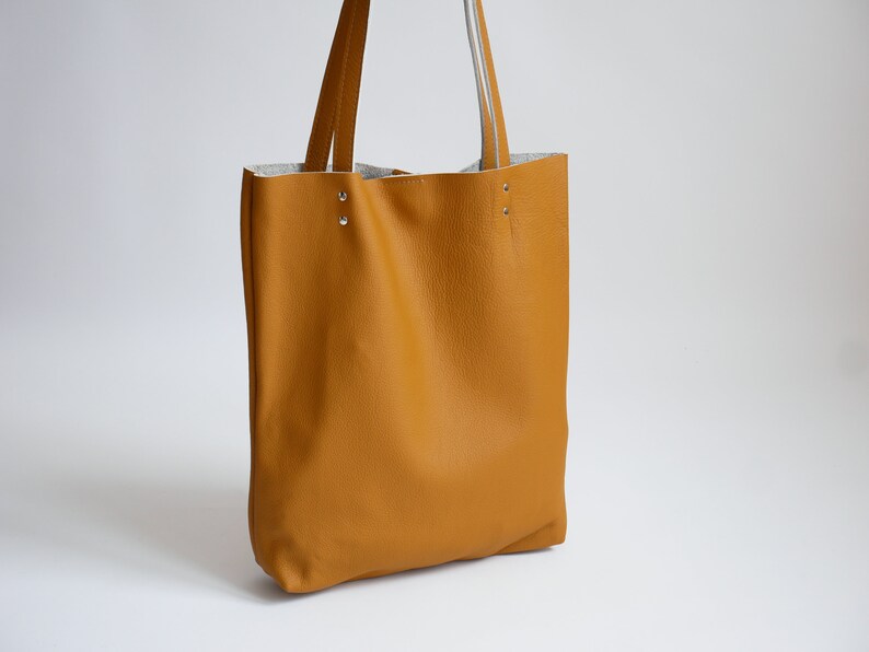 May include: A mustard yellow leather tote bag with two straps and silver rivets.