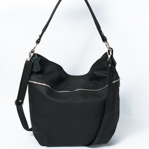 May include: A black nylon shoulder bag with a zipper closure and a silver zipper pull. The bag has a long adjustable strap and a small leather tag.