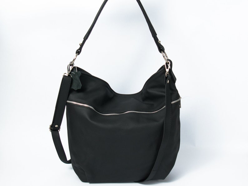 May include: A black nylon shoulder bag with a zipper closure and a silver zipper pull. The bag has a long adjustable strap and a small leather tag.