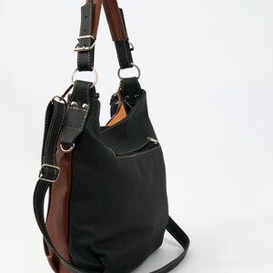 Puede incluir: Un bolso de mano de cuero negro con ribete de cuero marr&oacute;n y una correa larga para el hombro. El bolso tiene un bolsillo con cremallera en la parte delantera.