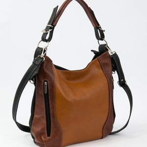 Puede incluir: Un bolso de mano de cuero marr&oacute;n con detalles negros y una correa larga ajustable. El bolso tiene un bolsillo con cremallera en la parte delantera y un cierre de solapa.