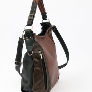 Pode incluir: Uma bolsa de ombro de couro marrom e preto com um bolso com z&iacute;per lateral. A bolsa tem uma al&ccedil;a longa que pode ser ajustada para ser usada no ombro ou transversalmente.