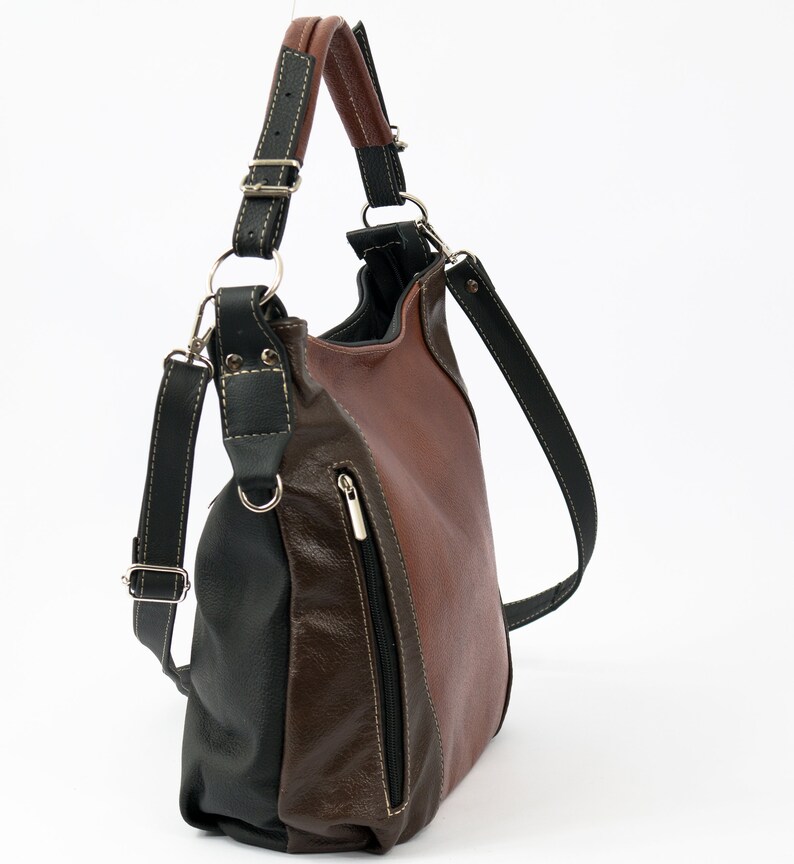 Pode incluir: Uma bolsa de ombro de couro marrom e preto com um bolso com z&iacute;per lateral. A bolsa tem uma al&ccedil;a longa que pode ser ajustada para ser usada no ombro ou transversalmente.