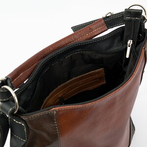 Pode incluir: Uma bolsa de m&atilde;o de couro marrom com uma al&ccedil;a de couro preto e um bolso com z&iacute;per. A bolsa est&aacute; aberta e o interior &eacute; forrado com tecido preto.