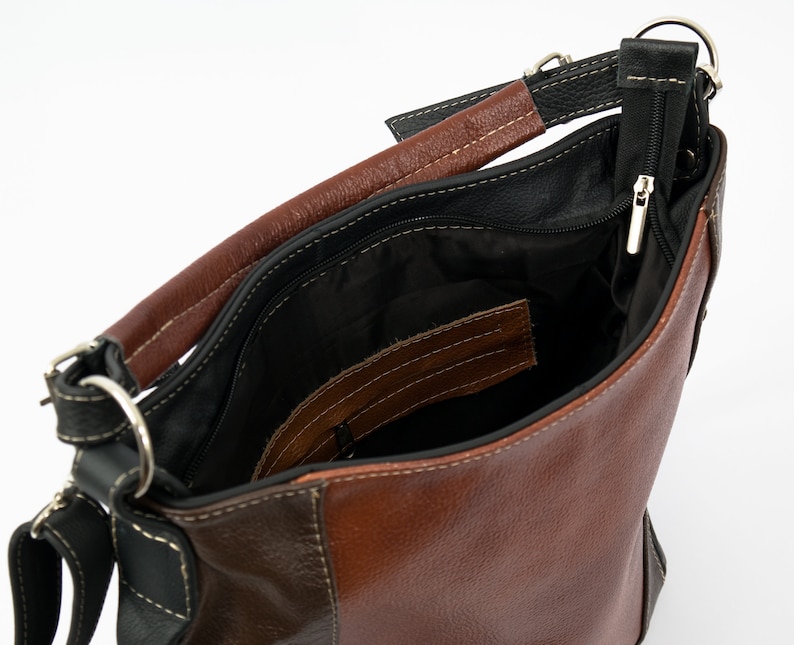 Pode incluir: Uma bolsa de m&atilde;o de couro marrom com uma al&ccedil;a de couro preto e um bolso com z&iacute;per. A bolsa est&aacute; aberta e o interior &eacute; forrado com tecido preto.