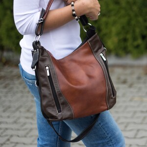Pode incluir: Uma bolsa de ombro de couro marrom e preto com um bolso com z&iacute;per e uma al&ccedil;a longa.