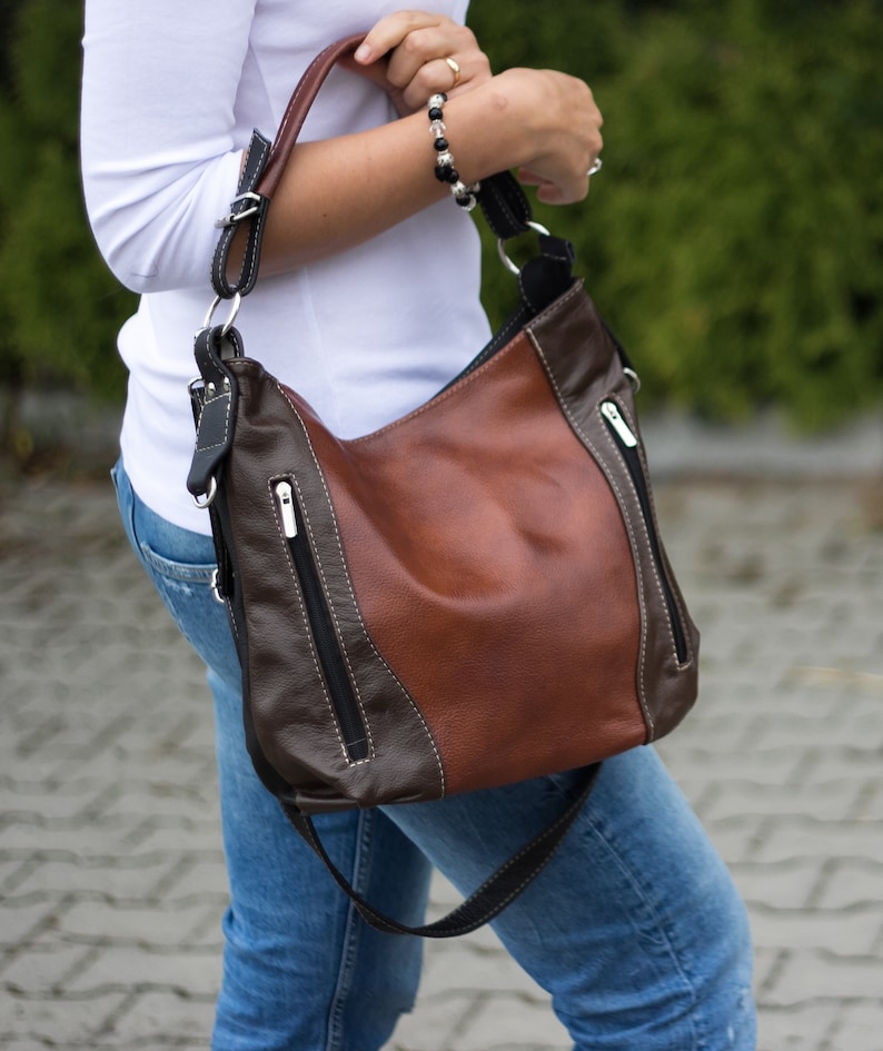 Pode incluir: Uma bolsa de ombro de couro marrom e preto com um bolso com z&iacute;per e uma al&ccedil;a longa.