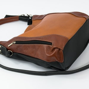 Puede incluir: Un bolso de mano de cuero marr&oacute;n y negro con una correa para el hombro. El bolso tiene un bolsillo con cremallera en la parte delantera.