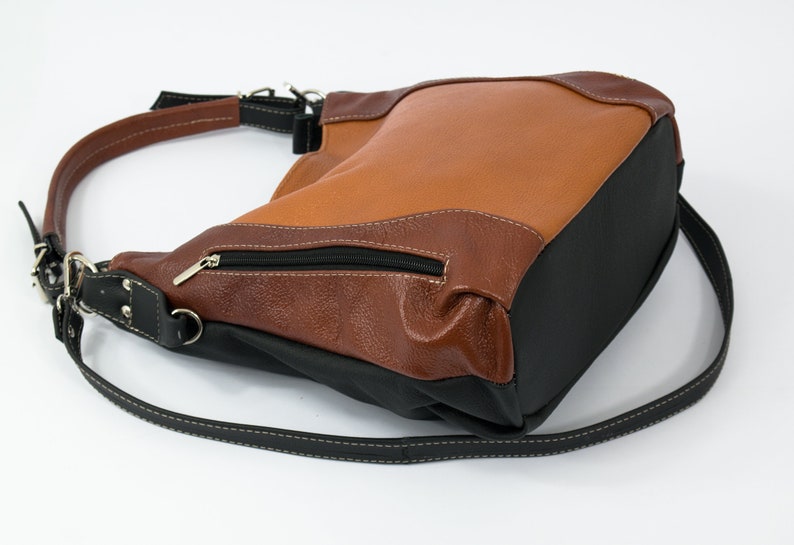 Puede incluir: Un bolso de mano de cuero marr&oacute;n y negro con una correa para el hombro. El bolso tiene un bolsillo con cremallera en la parte delantera.