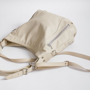 Peut inclure: Un sac &agrave; bandouli&egrave;re en cuir cr&egrave;me avec une poche zipp&eacute;e et des bretelles r&eacute;glables.