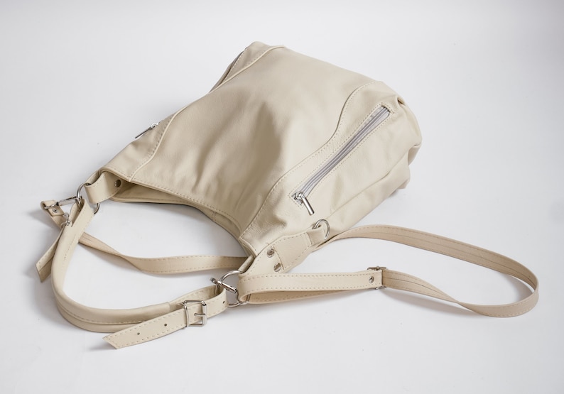 Peut inclure: Un sac &agrave; bandouli&egrave;re en cuir cr&egrave;me avec une poche zipp&eacute;e et des bretelles r&eacute;glables.