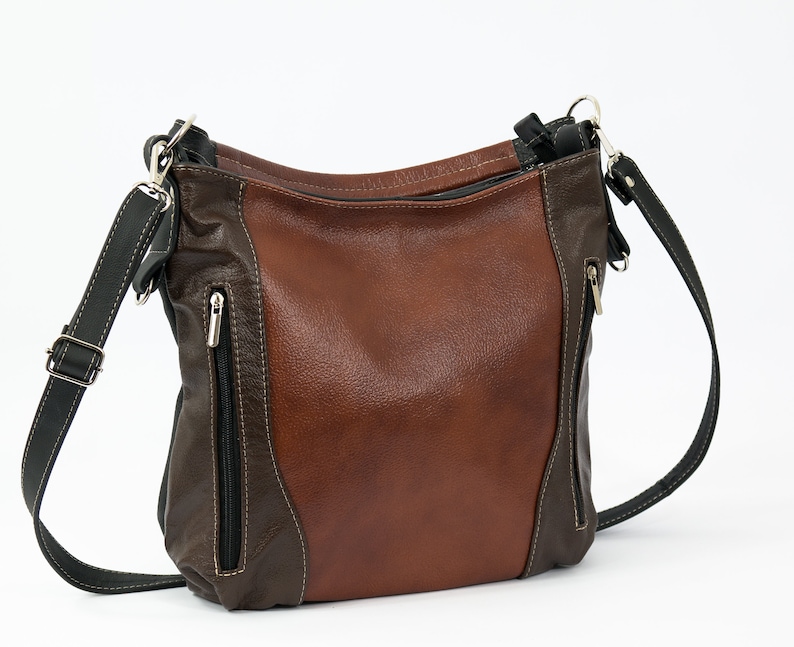 Pode incluir: Uma bolsa de ombro de couro marrom e preto com um bolso com z&iacute;per na frente. A bolsa tem uma al&ccedil;a longa ajust&aacute;vel.
