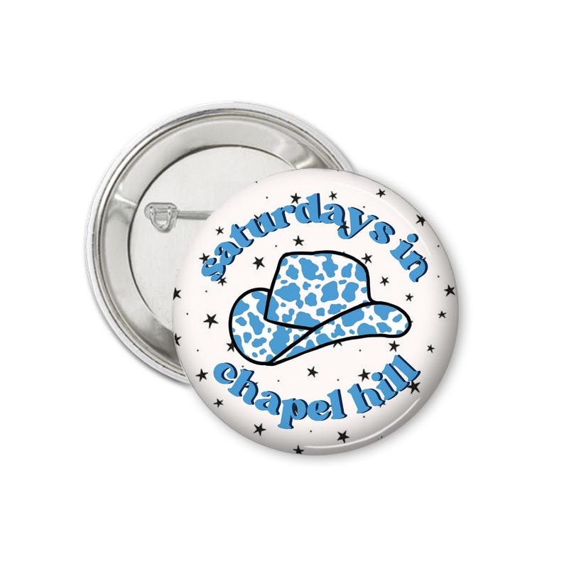 Peut inclure: Un badge blanc avec un chapeau de cowboy bleu et le texte "saturdays in chapel hill" en bleu. Le chapeau a un motif de vache. De petites &eacute;toiles noires entourent le design.