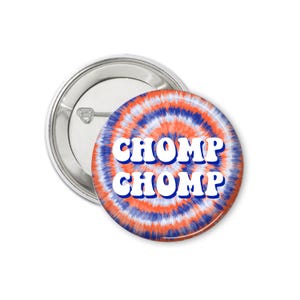 May include: A round button with a tie-dye pattern in shades of orange, blue, and white. The words "CHOMP CHOMP" are printed in white on the button.
