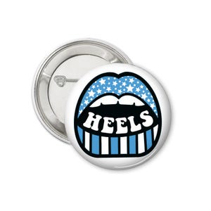 Peut inclure: Un bouton blanc avec un graphisme de l&egrave;vres bleues avec des &eacute;toiles blanches et des dents ray&eacute;es bleues et blanches. Le mot "HEELS" est en blanc, soulign&eacute; de noir. Un dos de bouton argent&eacute; est visible.