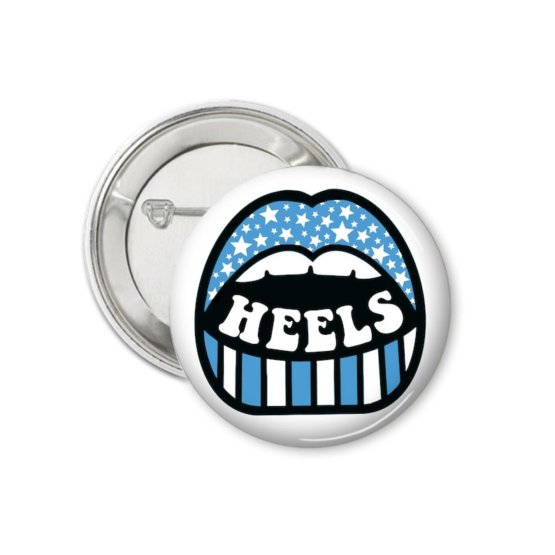 Peut inclure: Un bouton blanc avec un graphisme de l&egrave;vres bleues avec des &eacute;toiles blanches et des dents ray&eacute;es bleues et blanches. Le mot "HEELS" est en blanc, soulign&eacute; de noir. Un dos de bouton argent&eacute; est visible.