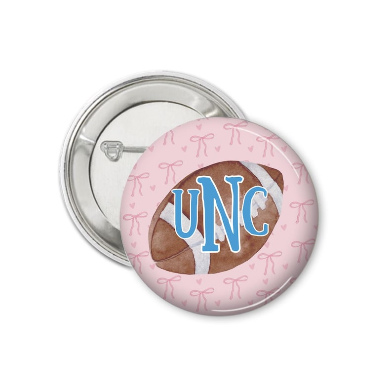 Peut inclure: Un bouton rond avec un fond rose repr&eacute;sentant un ballon de football aquarelle. Le ballon est marron avec des rayures blanches et les lettres "UNC" en bleu. Le fond pr&eacute;sente un motif de petits n&oelig;uds roses.