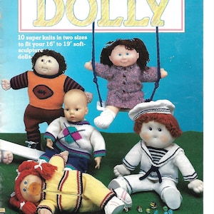 May include: A book cover with the title "Knit It For Dolly" and a picture of five dolls wearing knitted clothing. The dolls are sitting on a green grassy surface. The book cover is pink and blue with white text.