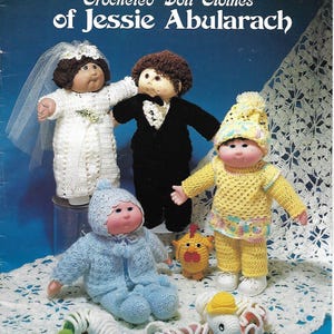 Puede incluir: Un libro titulado "Favorites & Originals Crocheted Doll Clothes of Jessie Abularach" que presenta cuatro atuendos de muñeca tejidos a crochet. Los atuendos incluyen un vestido de novia, un esmoquin, un atuendo amarillo con un sombrero y un atuendo de bebé azul. La portada del libro también presenta un encaje blanco tejido a crochet.