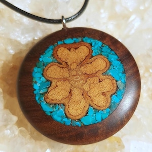 May include: A round wooden pendant necklace with a turquoise inlay in the shape of a flower. The pendant is brown with a light brown flower design.